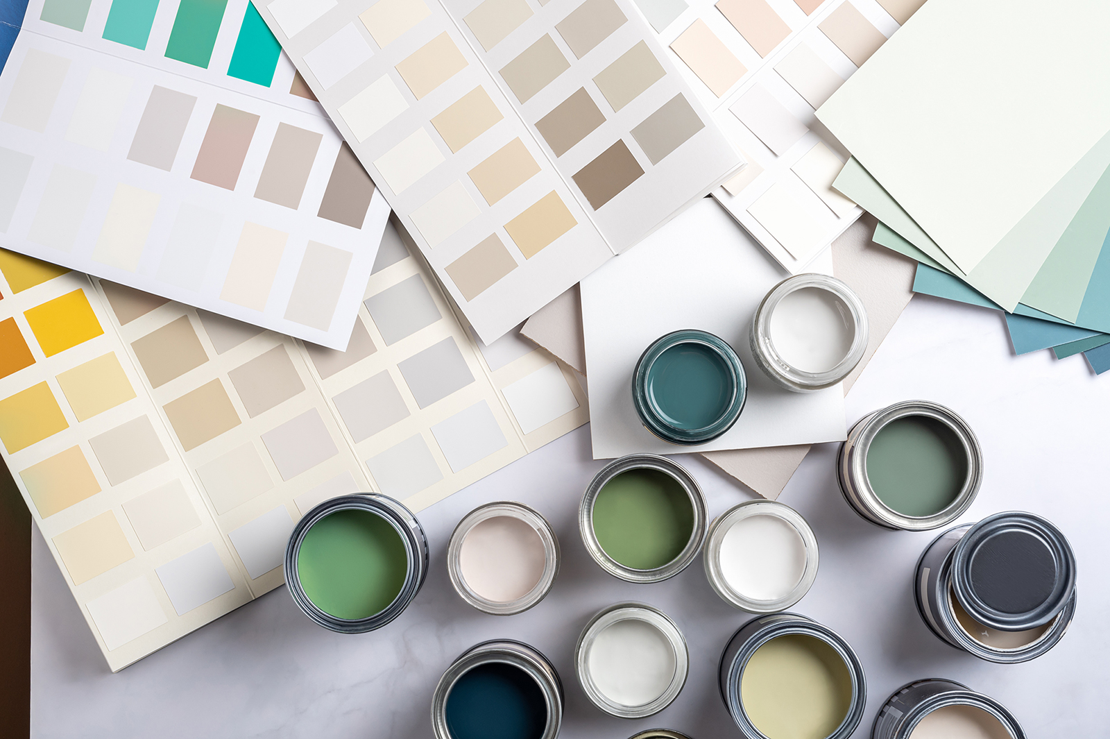 Tiny sample paint cans during house renovation, process of choosing paint for the walls, different green and beige colors, color charts on background